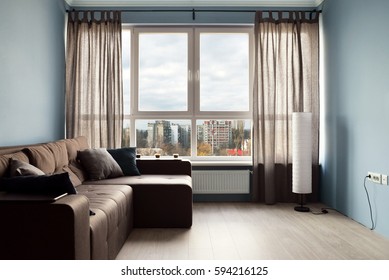 Clean Family Room With Brown Couch And Large Windows Showing Bright Spring Landscape In Background.