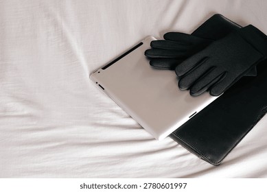 Clean flat lay image featuring a tablet device, black gloves, and a leather pouch arranged on soft white fabric. Modern minimalist composition ideal for technology, remote work, digital lifestyle, mobile productivity, travel essentials, personal accessories, cybersecurity concepts, and premium lifestyle branding