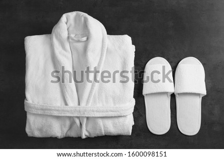 Clean folded bathrobe and slippers on black stone background, flat lay