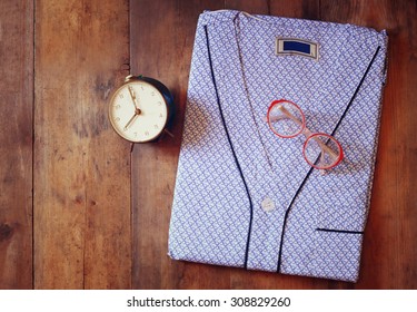 clean folded man's pajama, vintage clock and glasses over wooden background. top view - Powered by Shutterstock