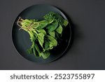 Clean food concept. Bunch of leaves of fresh organic spinach greens in a plate on a black background. Healthy detox spring-summer diet. Vegan Raw Food. Copy space.