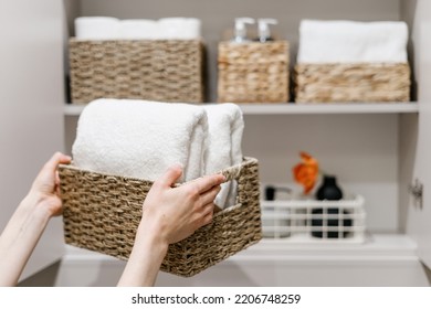 Clean fresh towels neatly folded and placed in closet organizer box. Woman putting wicker basket in bathroom wardrobe. Housework and housekeeping concepts. Selective focus on white laundry - Shutterstock ID 2206748259