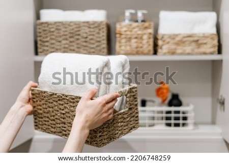 Clean fresh towels neatly folded and placed in closet organizer box. Woman putting wicker basket in bathroom wardrobe. Housework and housekeeping concepts. Selective focus on white laundry