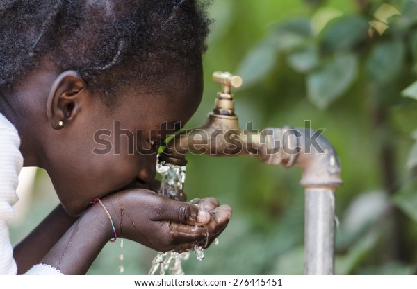 Clean Fresh Water Scarcity Symbol: Black Girl\
Drinking from Tap.\
\
Young African girl drinking clean water from\
a tap. Hands with water pouring from a tap in the streets of the\
city Bamako, Mali.