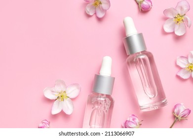 Clean glass cosmetic bottles with dropper, delicate spring flowers on pink background flat lay top view. Spring concept of natural organic cosmetics, beauty herbal product spa aroma oil. Mockup - Powered by Shutterstock