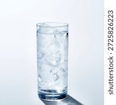 A clean, high-angle studio shot of a refreshing glass of mineral water filled with large ice cubes. The glass is covered in fresh condensation droplets, highlighting its cold temperature. Set against a minimalist bright white background with a soft shadow, perfect for health, wellness, or beverage advertising.