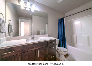 Clean home bathroom with toilet beside the shower area with drawn blue curtain