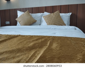Clean hotel double bed setup with white pillows, golden brown cushions, and bed runner