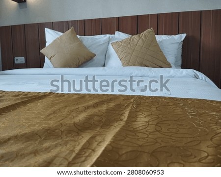 Clean hotel double bed setup with white pillows, golden brown cushions, and bed runner