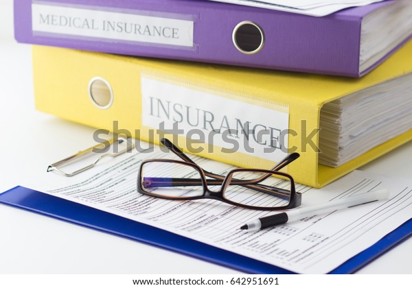 Clean insurance form on the plastic\
clipboard, folders, glasses and pen, soft focus\
background