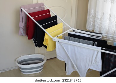 Clean laundry hanging on drying rack in room. Many or lots of washed laundry lined up to be dry. 