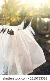 Clean Laundry White Clothes Hanging On Washing Line And Drying By Sunshine In The Wind In Garden Outdoor. Solar Energy. Yard Landscape Background. Clothespin On Rope. Ecological Way To Do Housework