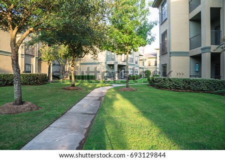 Clean lawn and tidy oak trees along the walk path through the typical apartment complex building in suburban area at Humble, Texas, US. Grassy backyard, sunset warm light.