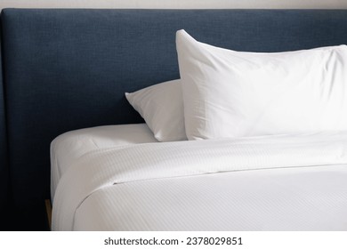 Clean, made hotel bed with white linens. Pillow, blanket on a bed with a soft headboard.