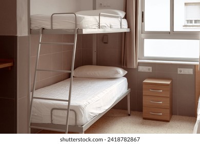 A clean and minimalistic hostel room with a bunk bed, white bedding, and a small wooden bedside table, ideal for budget travelers seeking affordable accommodation. Cheap hostels, save money.