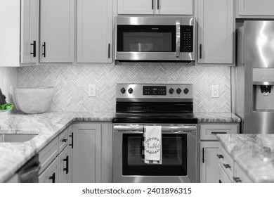 Clean Modern Kitchen Design with Stainless Steel Appliances and Herringbone Tile Backsplash Complemented by Grey Cabinets - Powered by Shutterstock