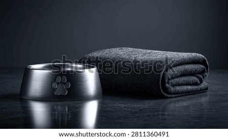 A clean, modern setup featuring a metallic pet bowl with a paw print emblem and a neatly folded dark towel, set against a dark, reflective background.