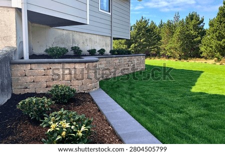 A clean and modern side yard design featuring a stone retaining wall, manicured green lawn, and minimalist landscaping. Perfect example of contemporary residential outdoor planning.