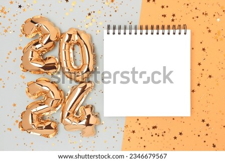 Clean notepad mockup, shimmer stars confetti and 2024 foil inflatable balloons on a blue and gold background. New Year resolutions concept.