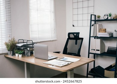 A clean and organized office with a desk, chair, and bookshelf. The desk has a laptop and a stack of papers. The room is well-lit and has a professional atmosphere - Powered by Shutterstock