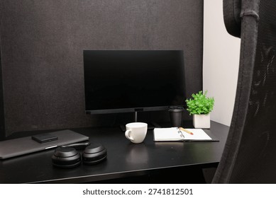 A clean and organized workspace featuring a computer monitor, noise-canceling headphones, a coffee cup, and a notebook with a pencil, perfect for remote work or study