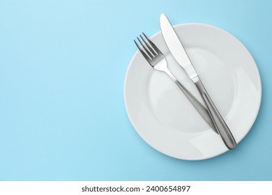 Clean plate, fork and knife on light blue background, top view. Space for text - Powered by Shutterstock