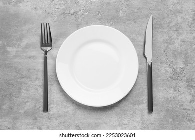 Clean plate and shiny silver cutlery on light grey table, flat lay