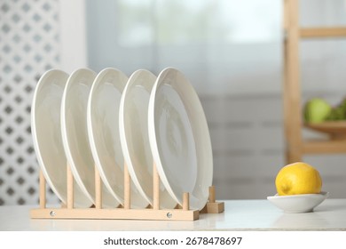 Clean plates in dish drying rack and lemon on white table indoors
