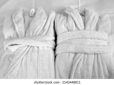 Clean, Ready For Use, Two White Terry Cloth Bathrobes Laying On White Sheet