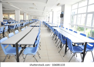 Clean School Cafeteria With Many Empty Seats And Tables.