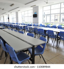 Clean School Cafeteria With Many Empty Seats And Tables.