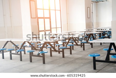 Clean school cafeteria with many empty seats and tables.
