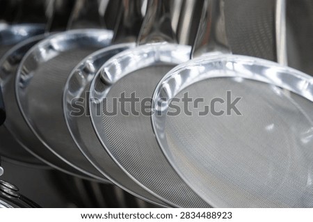 A clean, shallow depth-of-field shot capturing a neat row of hanging stainless steel wire mesh skimmer strainers with polished silver rims in an organized kitchen setup.