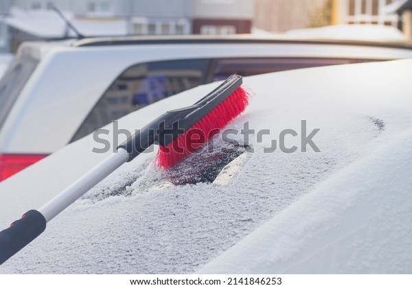 To clean snow with a brush from the\
windshield of a car after a snowfall in\
winter.