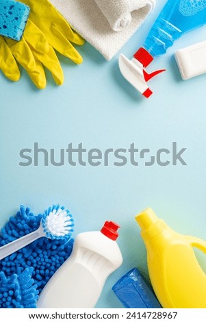 A clean sweep in aesthetics. Top view vertical photo featuring cleaning essentials—rags, gloves, and detergent bottles—arranged on calming pastel blue background. Adaptable space for text or branding