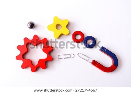 A clean top-down view of educational science tools including a red and blue horseshoe magnet attracting paperclips, wooden gear shapes, a yellow star, and a small metal sphere. Perfect for STEM education, physics concepts, or business metaphors regarding "attracting" success and mechanical synergy.