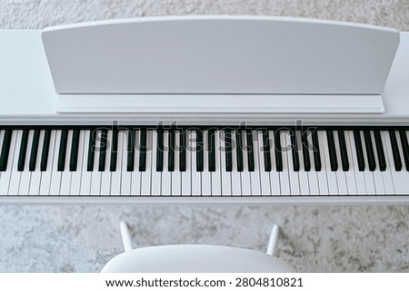 A clean, top-down view of a white digital piano, showcasing its keyboard and music stand, with a matching bench in the foreground.