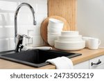 Clean washed tableware. Concept of washing dishes. Dishwashing liquid with brush, plates and cups near black kitchen sink with a chrome faucet on wooden counter and white subway tile backsplash