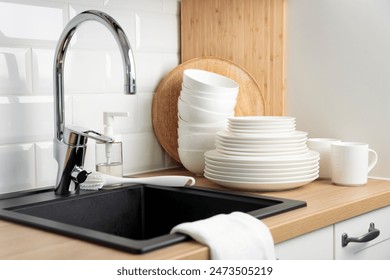 Clean washed tableware. Concept of washing dishes. Dishwashing liquid with brush, plates and cups near black kitchen sink with a chrome faucet on wooden counter and white subway tile backsplash