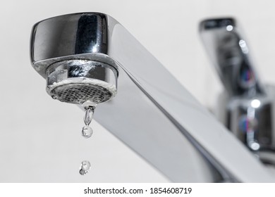 Clean Water Drop Falling From A Dripping Kitchen Faucet, An Unnecessary Waste Of Water. The Concept Of The Idea Of Saving Water.