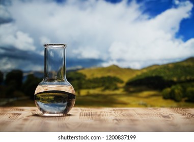 Clean water in a glass laboratory flask on wooden table on mountain background. Ecological concept, the test of purity and quality of water. - Powered by Shutterstock