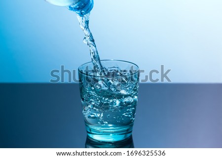Clean water is poured into a glass standing on a black table. Blue glass with flowing water standing on a black table on a blue background