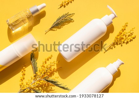 Clean white cosmetic containers bottles with mimosa flowers on yellow background flat lay top view. Blank label package for branding mock-up. Spring cosmetics concept. Natural organic beauty product