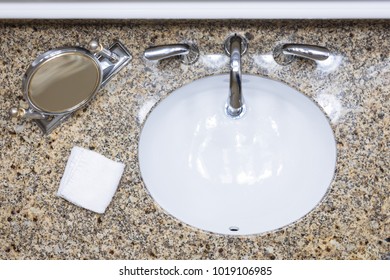 Clean White Sink, Silver Faucet, Makeup Mirror, White Washcloth On Granite Countertop Bathroom