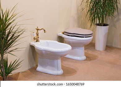 Clean and white toilet and bidet with gold-plated faucet in light bathroom. Beautiful bidet in luxurious bathroom