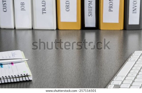 Clean working space with notepad, keyboard and\
folders. Clean and well ordered business working place with\
keyboard, notepad, colored folders. High contrast applied to\
highlight reflections of\
folders
