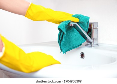 Clean up your house. Woman doing chores in bathroom, hands in yellow gloves cleaning of water tap, steel sink witth blue rag and detergent spray