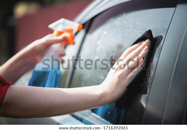 Cleaner is cleaning a car window glass with a rag and\
detergent close up.