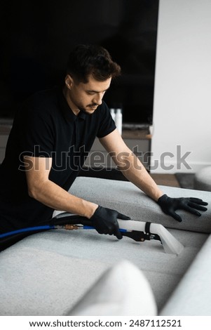 Cleaner is dry-cleaning sofa using extractor machine with detergent. Using extractor to refresh and clean from dust and stains upholstered furniture