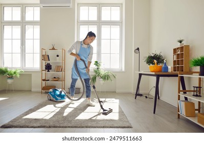 Cleaner, female homeowner tidying up at home, vacuuming carpet, floor in modern living room to perform household chores, doing nice housekeeping job using vacuum cleaner, home routine concept - Powered by Shutterstock